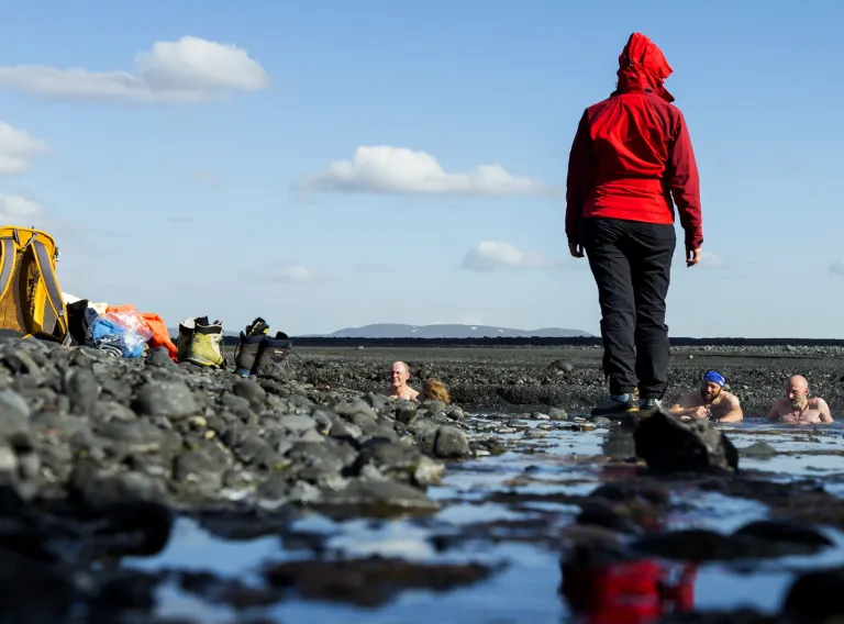 Tourists bating in a hot spring. Tour guide in red coat talking to them.