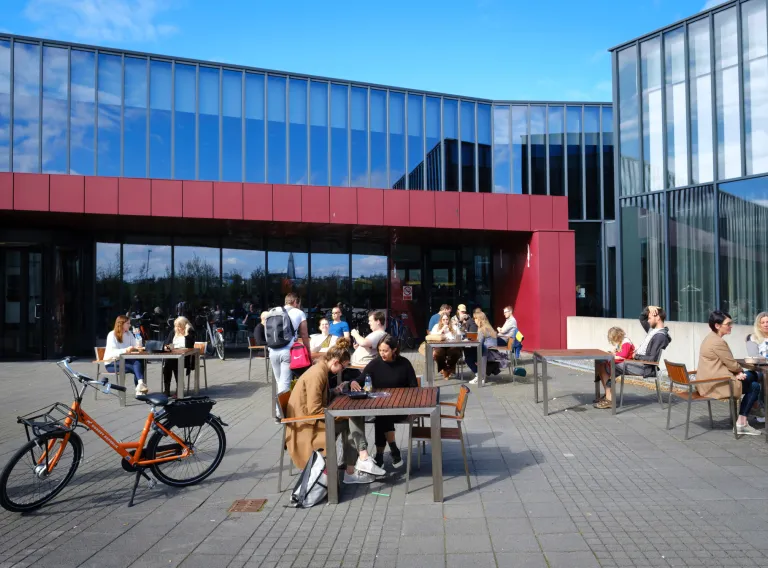 People sitting around tables in front of University Centre.