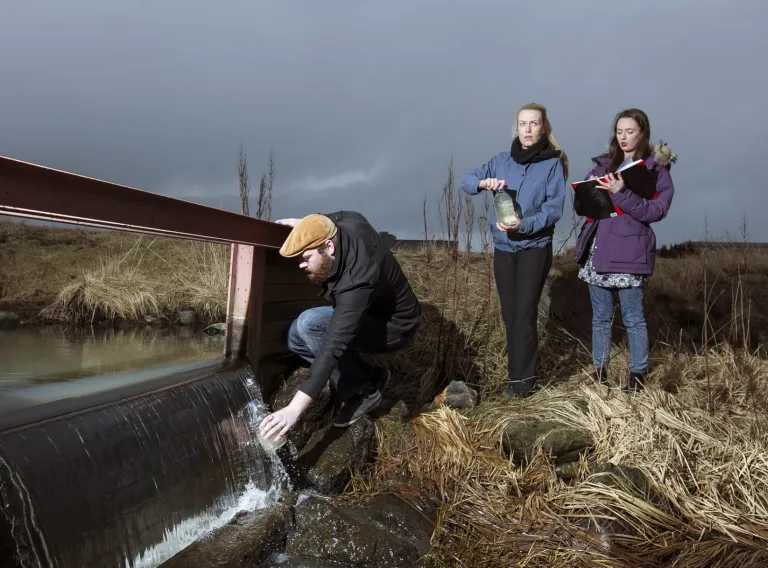 Students in the nature taking sample of water from a spring.
