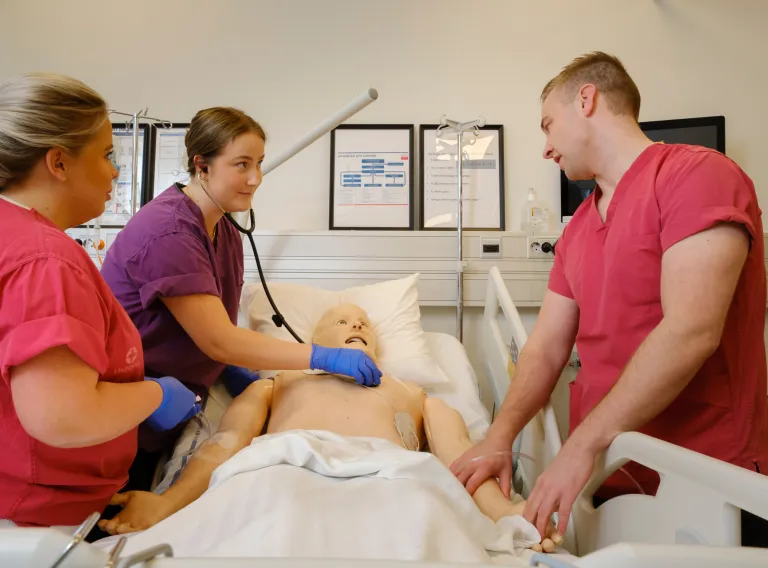 Students practice on a medical doll patient.