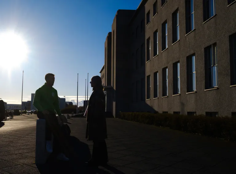 Two people in silhouette in front of main building, sun is shining.