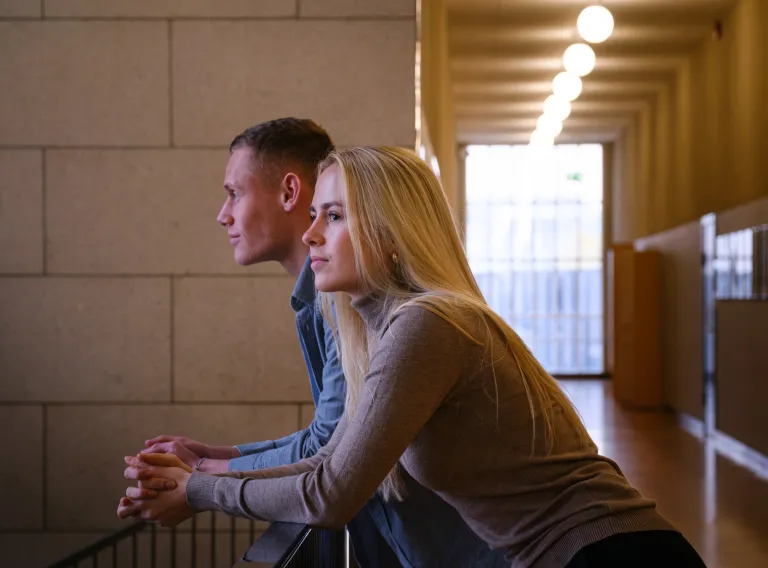 Two students man and woman leaning over handrail.