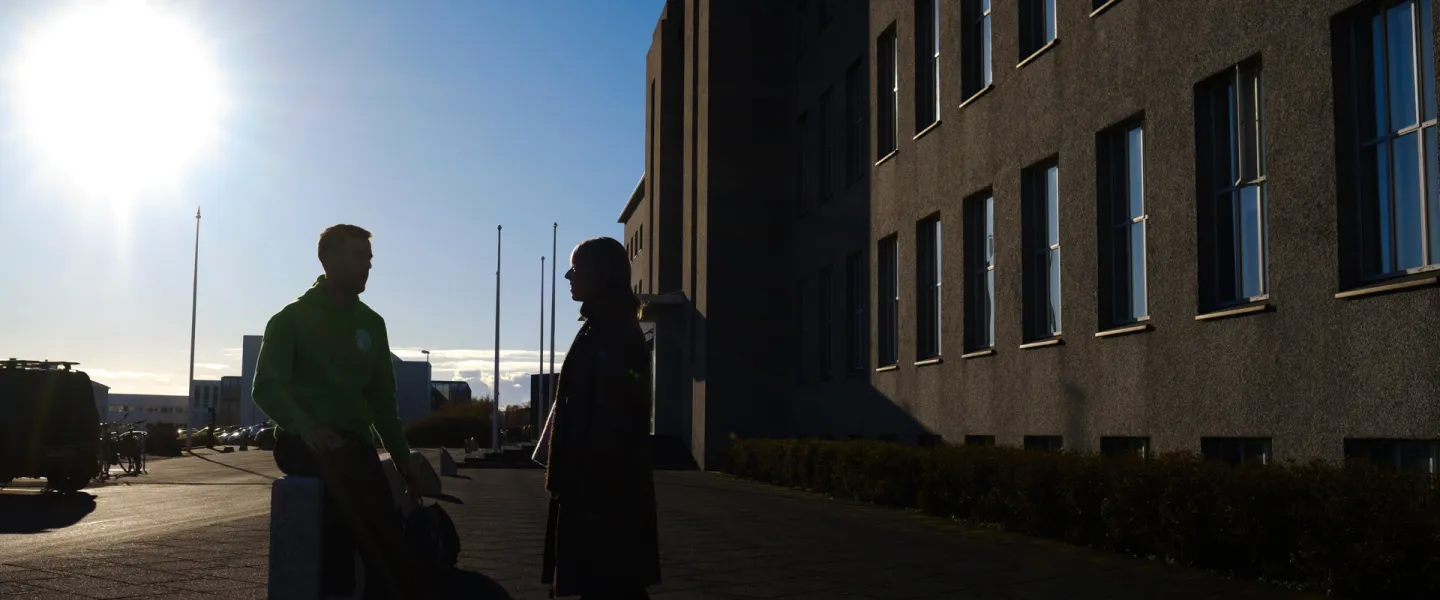 Two people in silhouette in front of main building, sun is shining. 