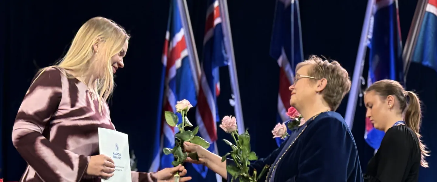 Silja Bára R. Ómarsdóttir, Rector of UI, handing a rose to a graduate at the graduation ceremony.