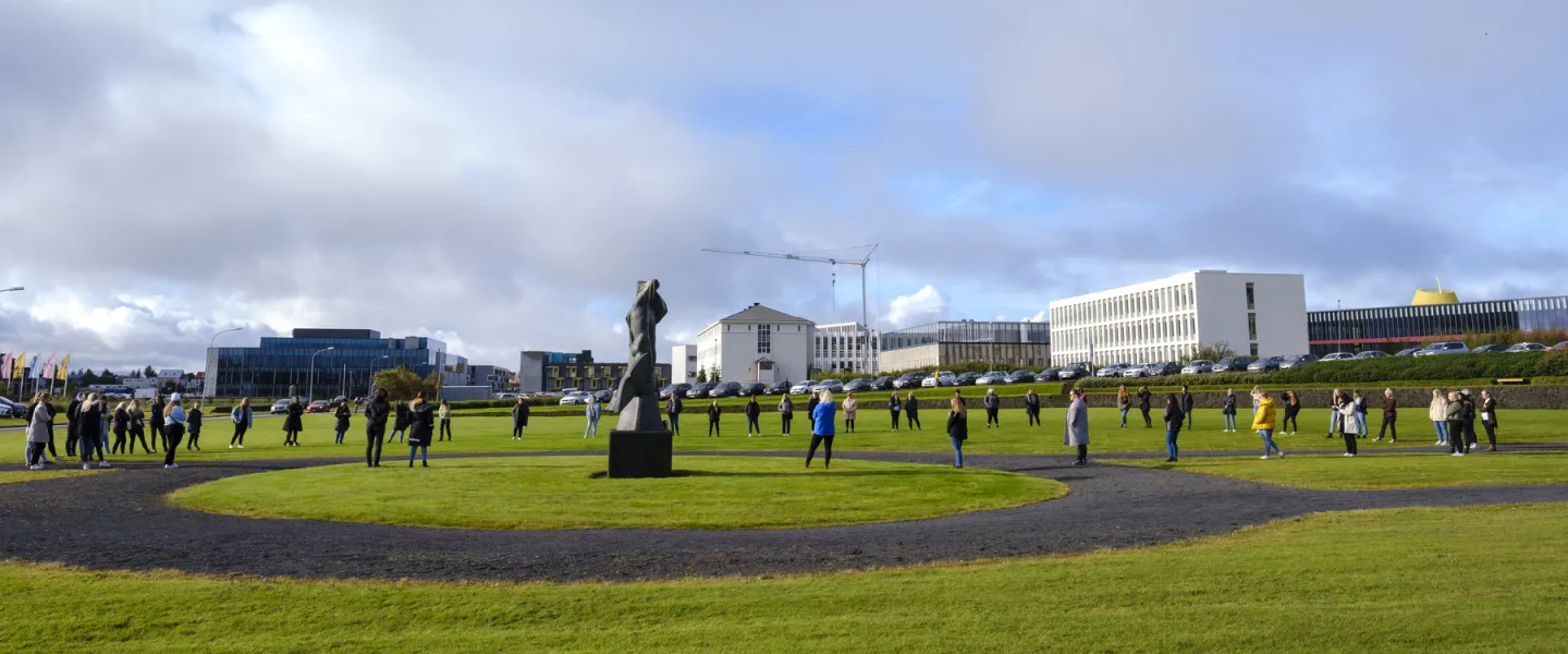 People standing on the grass in Skeifan outside of University of Iceland main Building