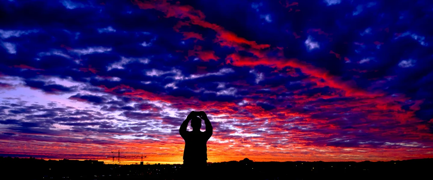 Silhouette of a man taking picture of the sunrise in Reykjavík. Perlan in the background