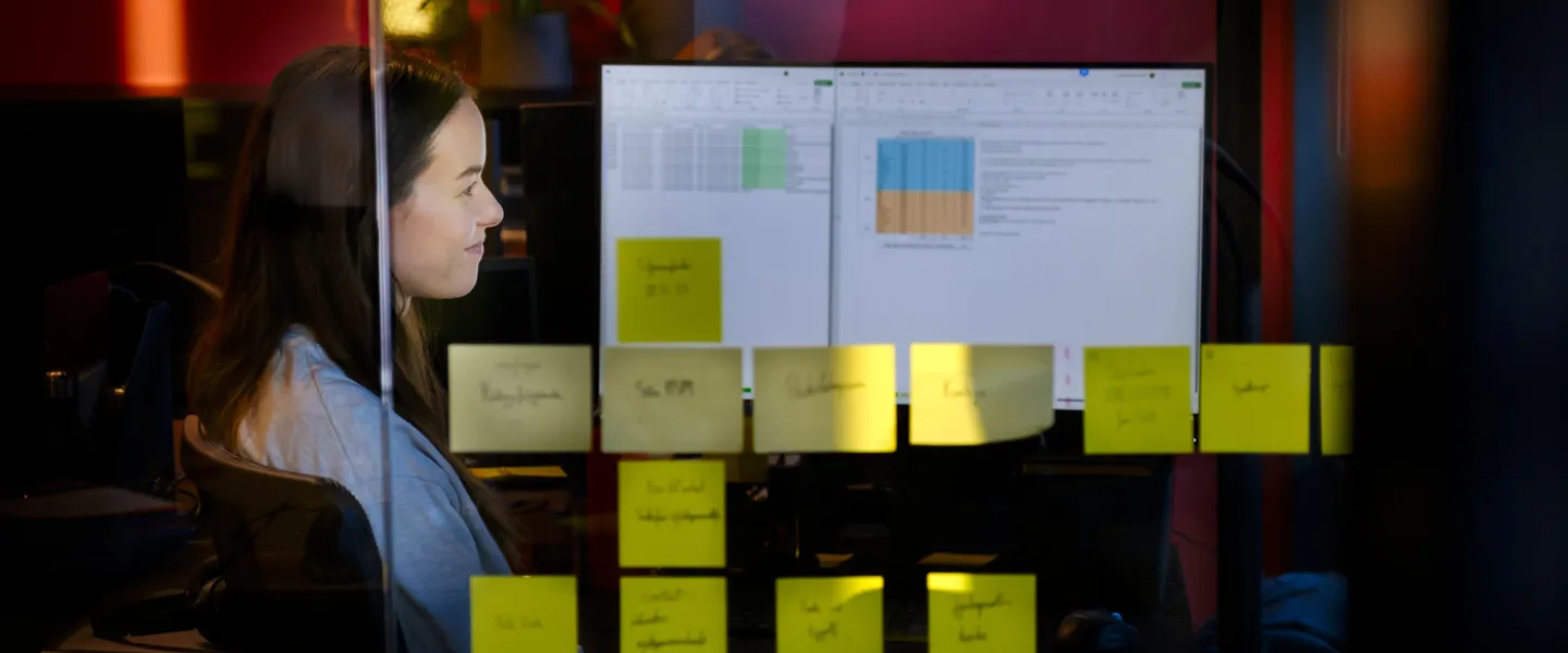 Woman sitting in front of acomputer, post-it-notes on a window