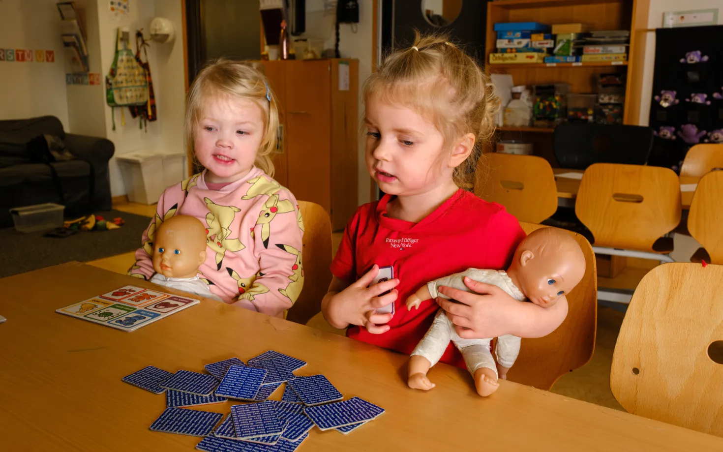 Two girls playing with dolls and cards