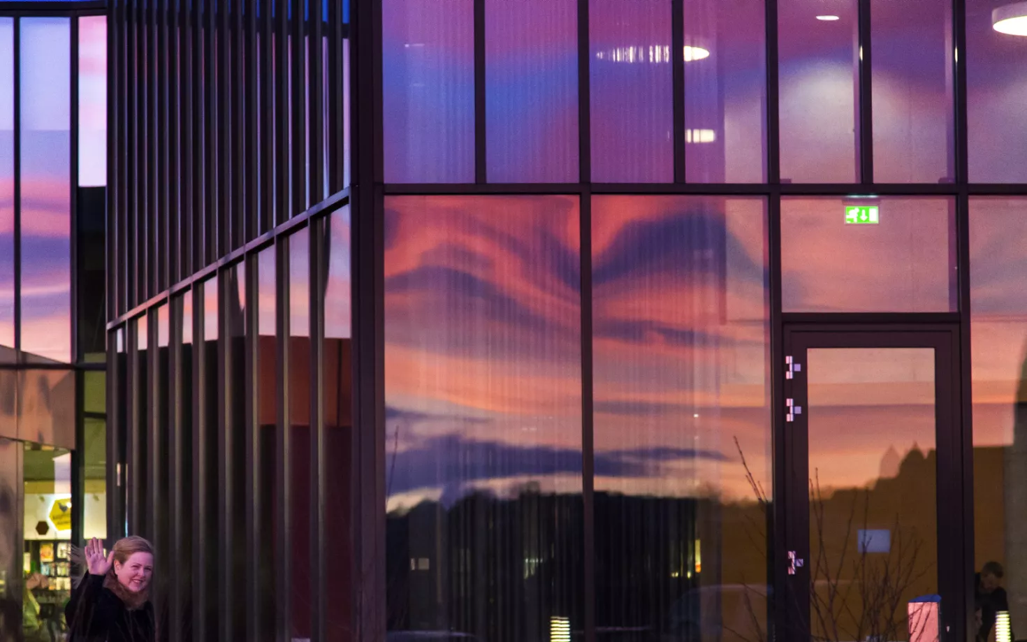 Outside University Centre, at University of Iceland. Sky reflecting in the windows. Woman waving at the camera