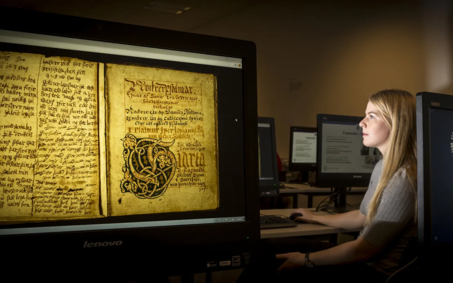 Woman sitting in front of a computer screen showing picture of an old manuscript