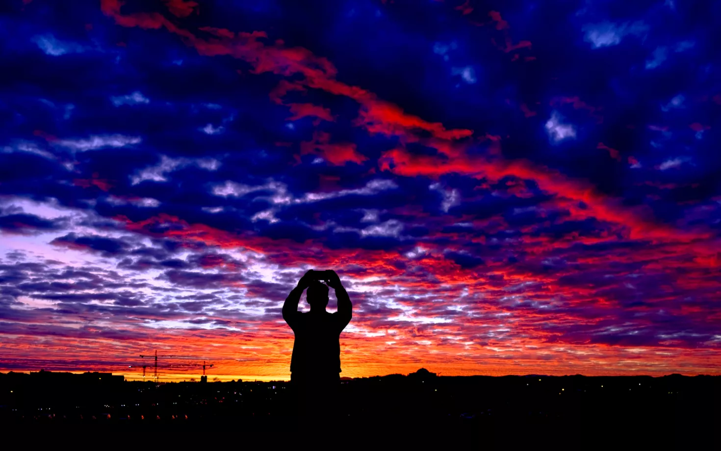 Silhouette of a man taking picture of the sunrise in Reykjavík. Perlan in the background