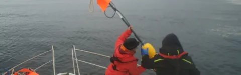 Two people on a boat, putting a Marine Vibrator into the ocean.