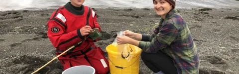 Two researcher with a yellow bucket, collecting samples at shore