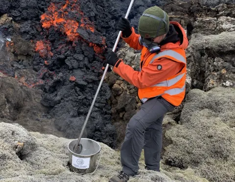 Man collecting a sample of molten lava by cooling it in a bucket of water.