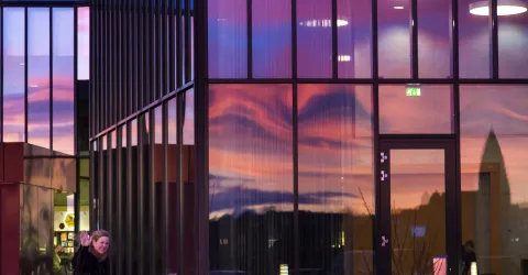 Outside University Centre, at University of Iceland. Sky reflecting in the windows. Woman waving at the camera
