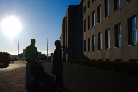 Two people in silhouette in front of main building, sun is shining. 