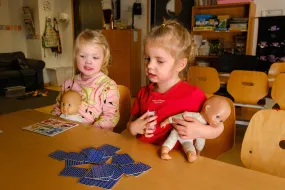 Two girls playing with dolls and cards