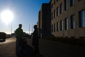 Two people in silhouette in front of main building, sun is shining. 