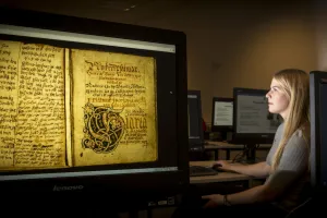 Woman sitting in front of a computer screen showing picture of an old manuscript